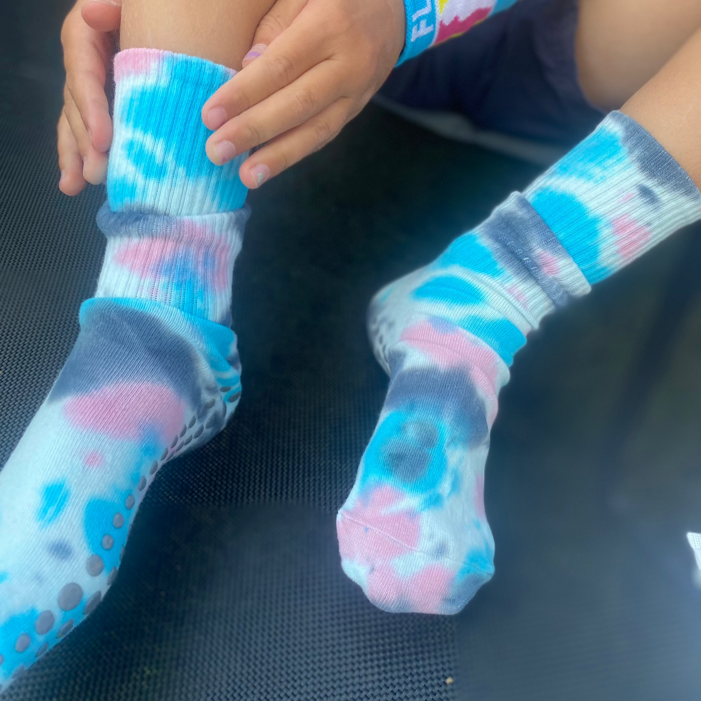 A child adjusting tie-dye grip socks sat on a trampoline.