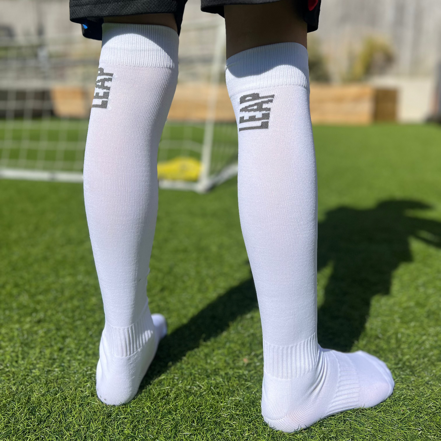 Knee high white fooball socks on a child model showing the LEAP logo.